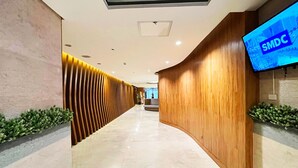 A modern reception area with a curved wooden reception desk, a digital display, and a patterned wall. - Shore 2 Residences (Pasay)