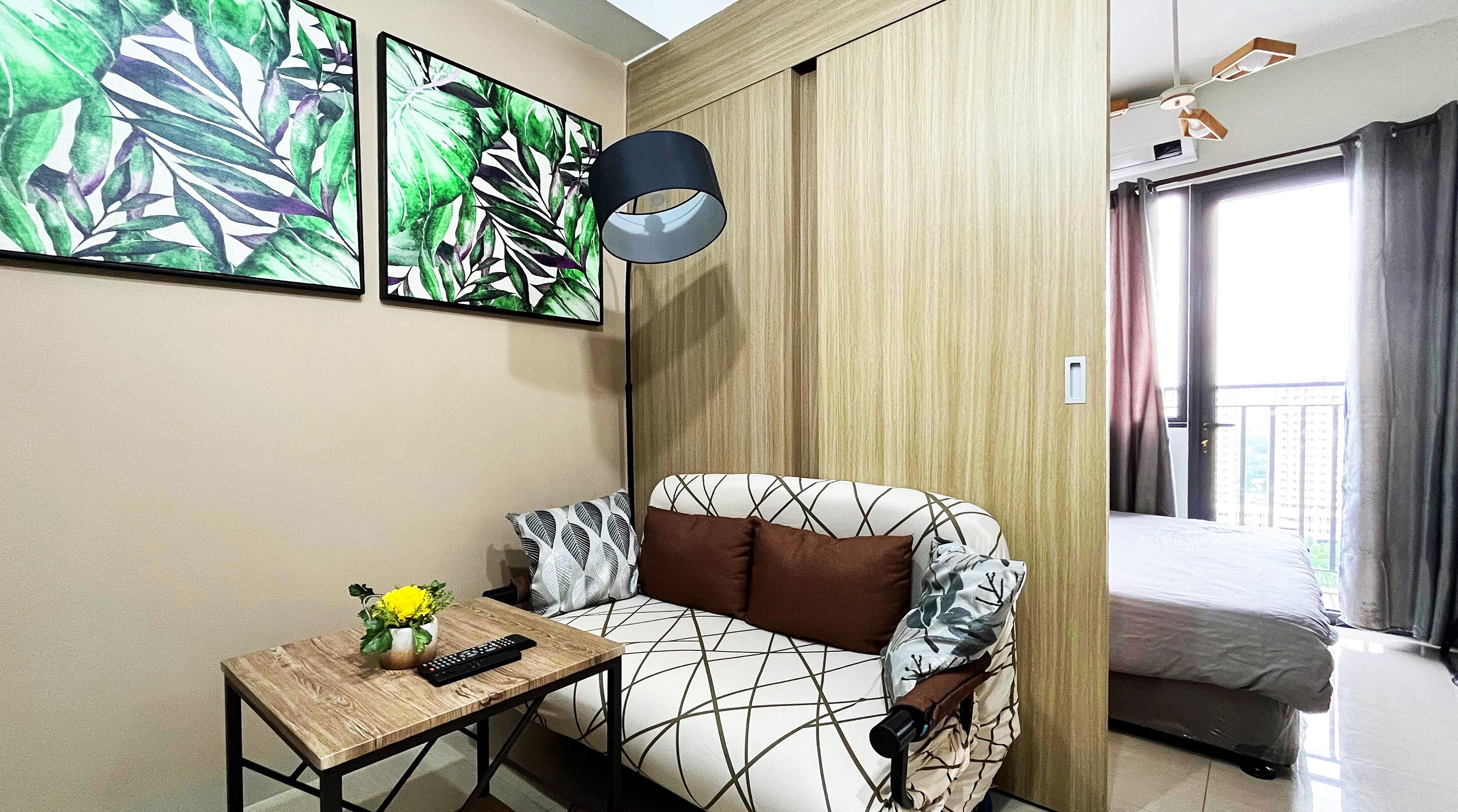 A modern hotel room with a sofa, a small table with a remote control, and a window with curtains.