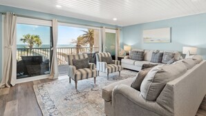A spacious living room with a large window, a balcony, and a view of the ocean.