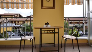 Ein Balkon mit Tisch und zwei Stühlen, eine herzförmige Dekoration an der Wand und Blick auf Gebäude und parkende Autos.