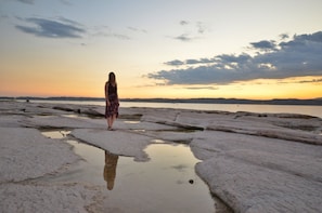 A person standing on a rocky beach with a body of water in the background. - Sirmione House: (Sirmione)
