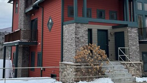A two-story building with a stone chimney, red siding, and a green roof. - Hunter Mountain 2 Bedroom Condo - Steps to Ski Slopes!! (Hunter)