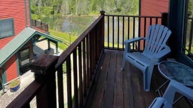 A red building with a wooden deck, white chairs, and a view of a lake and hills. - Hunter Mountain 2 Bedroom Condo - Steps to Ski Slopes!! (Hunter)