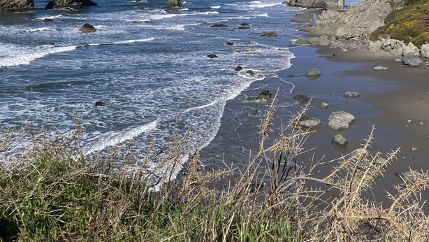 A coastal landscape with rocky outcrops and waves crashing onto the shore.