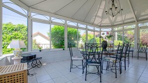 A sunroom with large windows, a chandelier, and a dining area with chairs and a table. - La Ribambelle - Saint Hilaire Sous Romilly (SAINT HILAIRE SOUS ROMILLY)