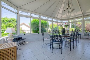 Un solarium con ventanas amplias, una araña y un comedor con sillas y una mesa.