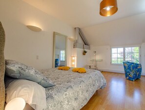 A bedroom with a large bed, a mirror, a small table, and a chair.