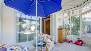A sunlit room with a large window, a blue umbrella, a floral sofa, a wooden cabinet, and children's toys. - La Ribambelle - Saint Hilaire Sous Romilly (SAINT HILAIRE SOUS ROMILLY)