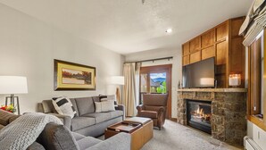 Una sala de estar con un sofá gris, un sillón marrón, una chimenea y un televisor.