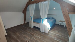 A bedroom with a wooden ceiling, a bed with blue bedding, and a nightstand. - LA Chaira - Neufmanil (NEUFMANIL)
