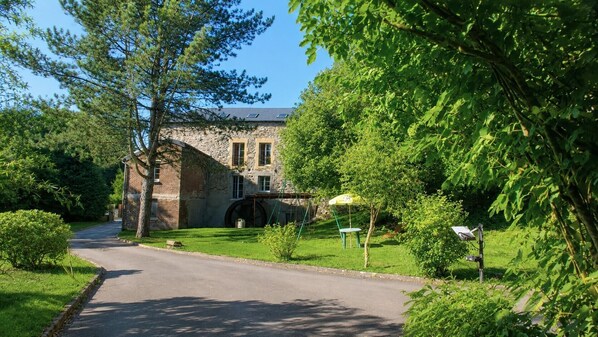 A stone building with a large wheel, a paved road, and lush greenery. - LA Goutelle - Neufmanil (NEUFMANIL)