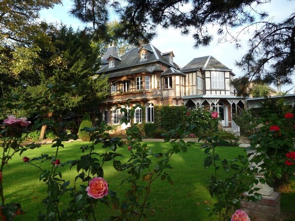 A large, two-story house with a traditional architectural style, surrounded by a well-maintained garden with various plants and flowers.