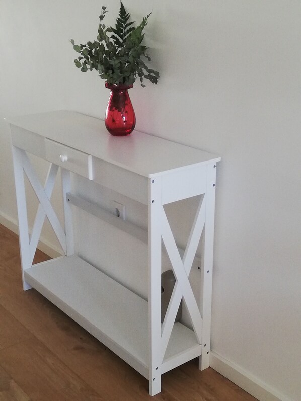 A white metal console table with a red vase and green foliage on top.