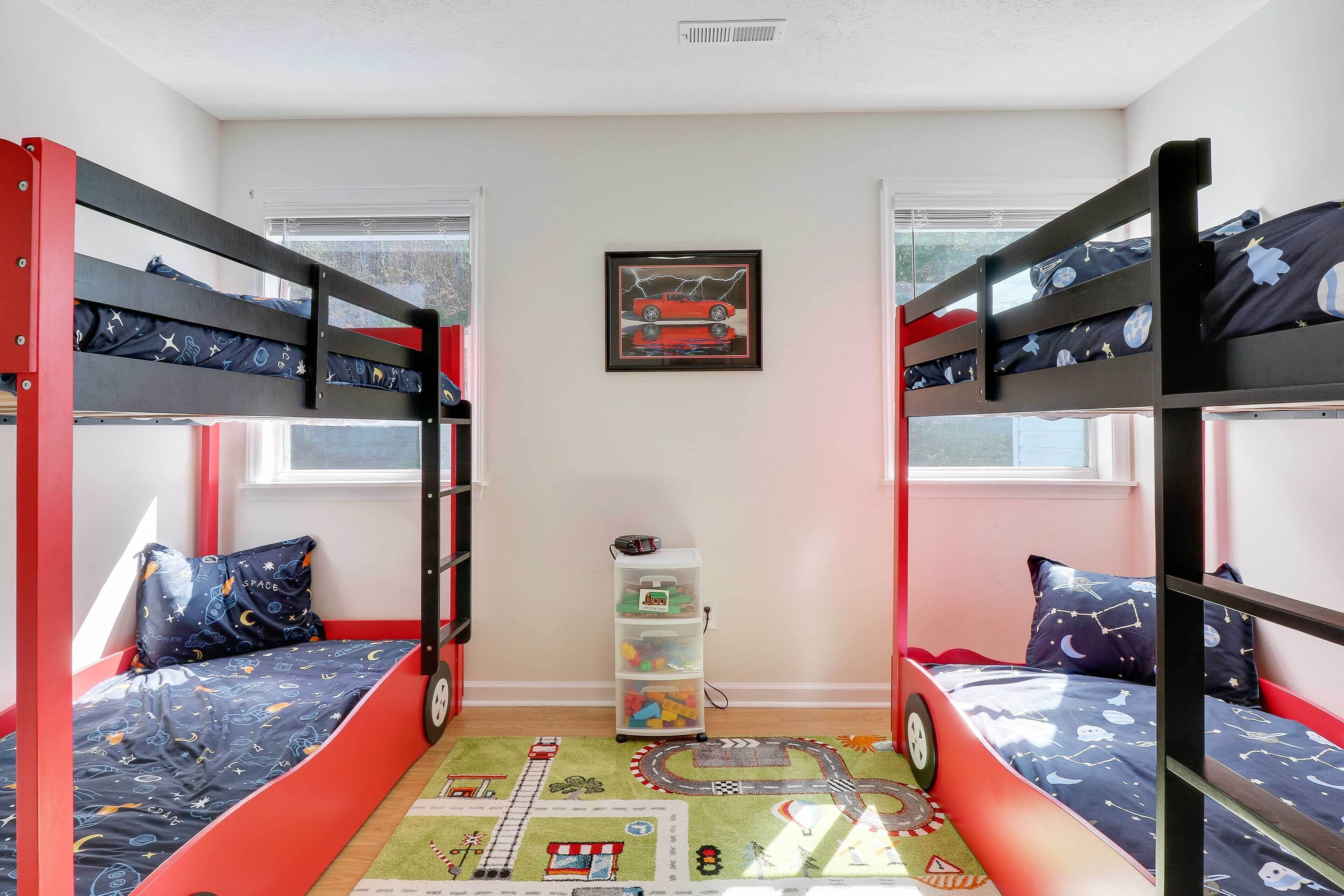 Een slaapkamer met een stapelbed, een speelmat, een opbergmeubel en een ingelijst beeld aan de muur.
