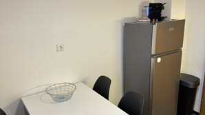 A compact kitchen with a white table, black chairs, a stainless steel refrigerator, and a small trash bin. - Gemütliche Ferienwohnung im Grünen (Alsfeld)