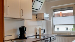A kitchen with white cabinets, a microwave, a coffee maker, and a window with blinds. - Gemütliche Ferienwohnung im Grünen (Alsfeld)