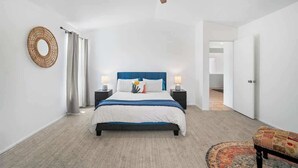 Una camera da letto con un letto, comodini, una ventola a soffitto, uno specchio rotondo e una panca decorata.