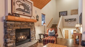 A cozy living room with a stone fireplace, a plaid armchair, and a wooden coffee table.
