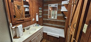 Een houten badkamer in cottage-stijl met een dubbele wastafel, een spiegel, een handdoekhouder en een bad.