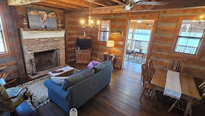 Ein gemütliches Blockhaus-Interieur mit Kamin, Holzwänden, einer Couch, einem Esstisch und einem Fernseher.