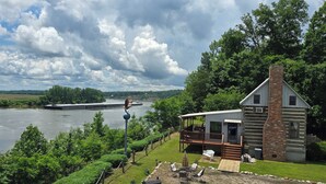 Eine Hütte mit einer Terrasse, die auf einen Fluss mit üppigem Grünblick blickt.