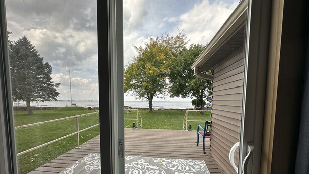 Vue depuis une pièce dotée d’une grande fenêtre donnant sur une terrasse agrémentée d’un tapis à motifs, d’un arbre et d’une pelouse.