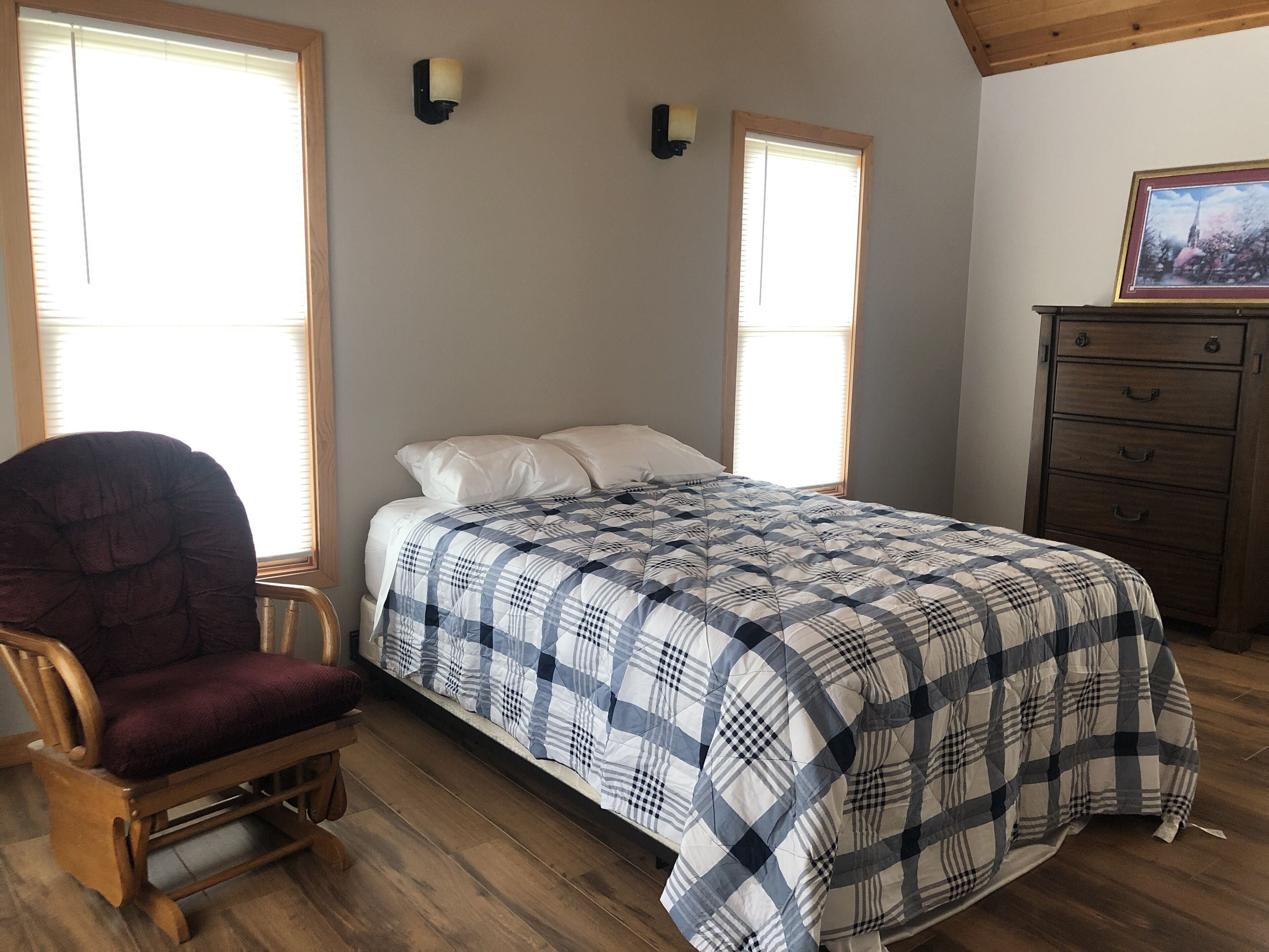 A bedroom with a bed, a wooden chair, a dresser, and two wall-mounted lights.