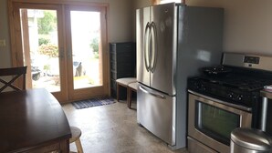 Een kleine keuken met een koelkast, fornuis en een eethoek met een tafel en stoelen.