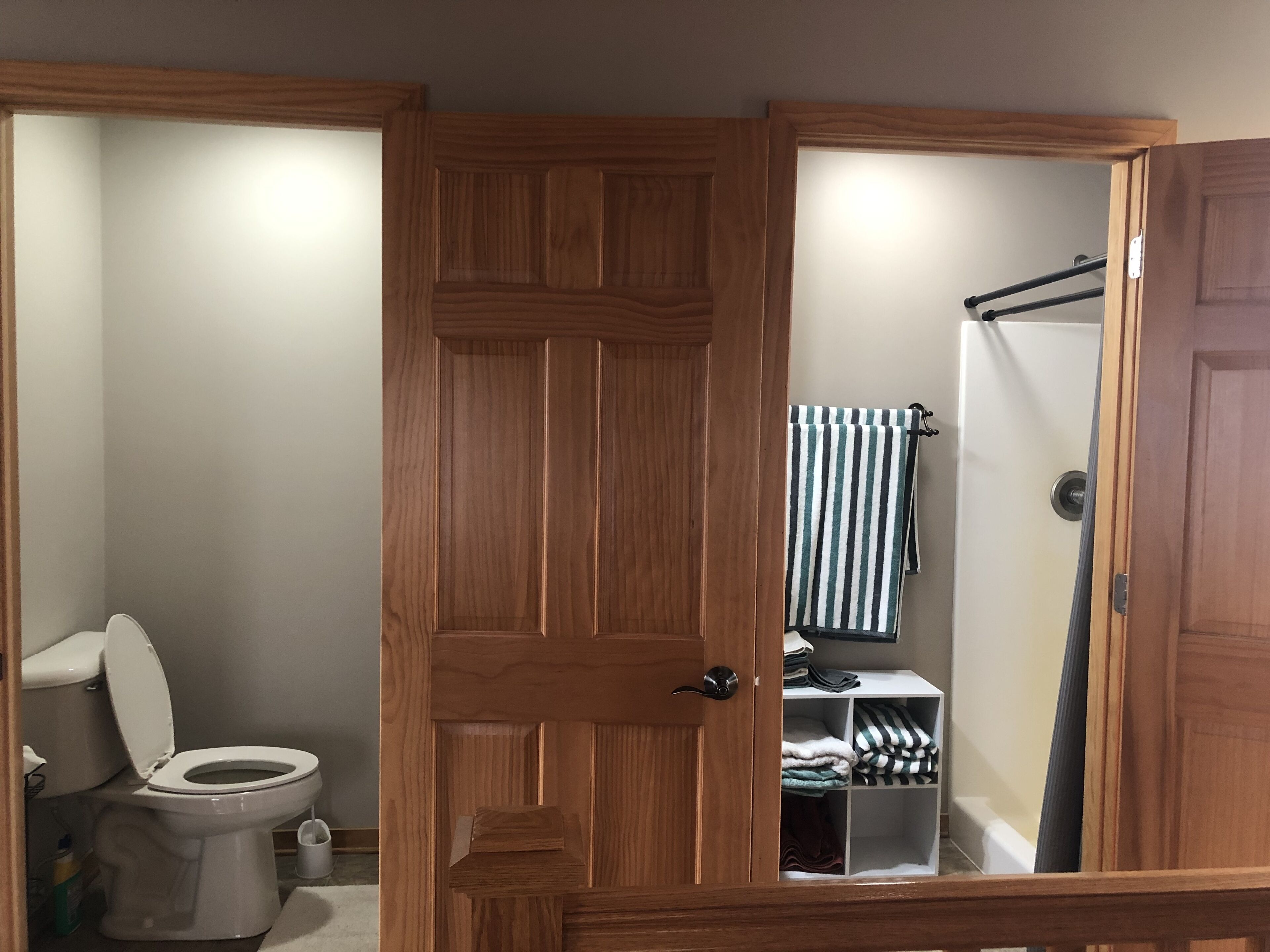 Ein Badezimmer mit Holztür, Toilette, Dusche und Handtuchhalter.