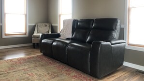 Een woonkamer met een zwarte leren fauteuil, een gestreept fauteuil en een rood-beige vloerkleed.