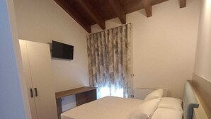 A bedroom with a bed, a nightstand, a TV mounted on the wall, and a window with curtains. - Elegant standard room in Riccia (Molise)