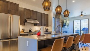 Une cuisine moderne dotée d’un grand îlot central, d’appareils électroménagers en acier inoxydable et de luminaires suspendus.