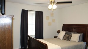 A bedroom with a wooden bed, a ceiling fan, and a window with curtains.