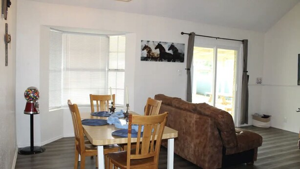 A dining area with a wooden table and chairs, a brown sofa, and a window with blinds.