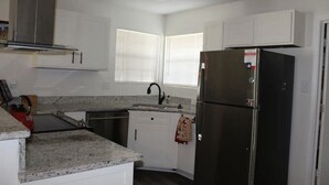A compact kitchen with white cabinets, a stainless steel refrigerator, a built-in oven, and a granite countertop.
