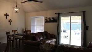 A living room with a brown leather couch, a dining table with chairs, a ceiling fan, and a large sliding glass door leading to an outdoor area.