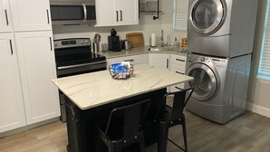 Een compacte keuken met witte kastjes, een ingebouwde magnetron, een kookplaat, een spoelbak en een gestapelde wasmachine en droger.