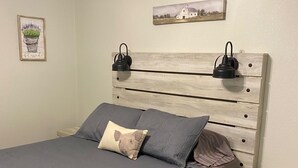 Een slaapkamer met een bed, nachtkastje, hoofdbord, een wandlamp en een ingelijste foto.