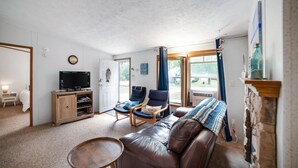 A cozy living room with a leather sofa, two armchairs, a television, and a fireplace. - Quaint Cabin: Beach Days & Bonfire Nights – The Ultimate Summer Escape! No Central A/C (Oscoda)