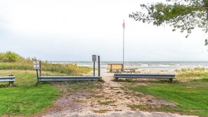 A gravel path leading to a beach with benches and a sign indicating no parking or standing. - Quaint Cabin: Beach Days & Bonfire Nights – The Ultimate Summer Escape! No Central A/C (Oscoda)