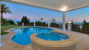 A swimming pool with a hot tub, surrounded by a fence and palm trees, with a view of the city in the background. - Colina del Mar, un Magnífico Jardín con Piscina y Maravillosas Vistas (Benalmádena)