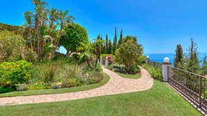 A landscaped garden with a stone pathway leading to a gate, surrounded by various plants and trees. - Colina del Mar, un Magnífico Jardín con Piscina y Maravillosas Vistas (Benalmádena)