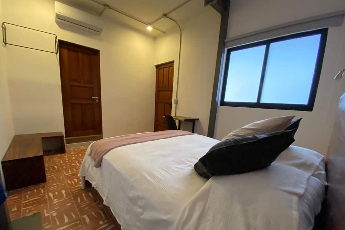 Quarto com cama, janela, porta e ar-condicionado.