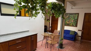 A kitchen with wooden cabinets and a granite countertop, a dining area with wicker chairs, a blue sofa, and a potted plant. - C. Santos Degollado 34 (Colima)