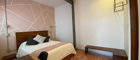 Una habitación de hotel con cama, mesita de noche y un banco.