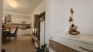 A modern kitchen with white cabinetry, a dining area with a table and chairs, and a decorative plant arrangement on the counter. - Holiday apartment mit Terrasse und Klimaanlage (Šilo)