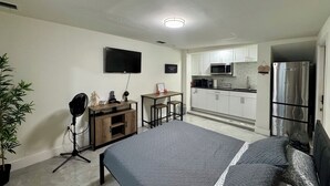 Een compact studio-appartement met een bed, kitchenette en een aan de muur bevestigde televisie.