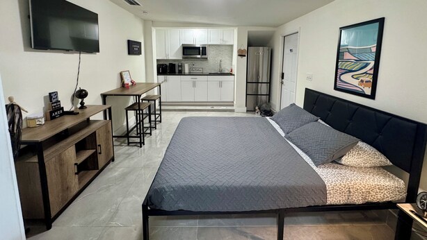 Een slaapkamer met een bed, een bureau en een kitchenette op de achtergrond.