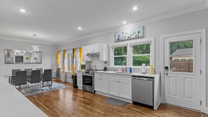 Une cuisine moderne avec des meubles blancs, un coin repas comprenant une table et des chaises, et une grande fenêtre donnant sur un paysage verdoyant.