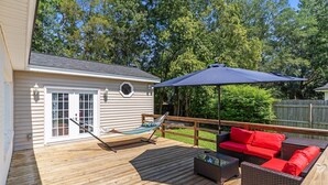 Une terrasse en bois avec un hamac, un canapé rouge et un grand parasol.